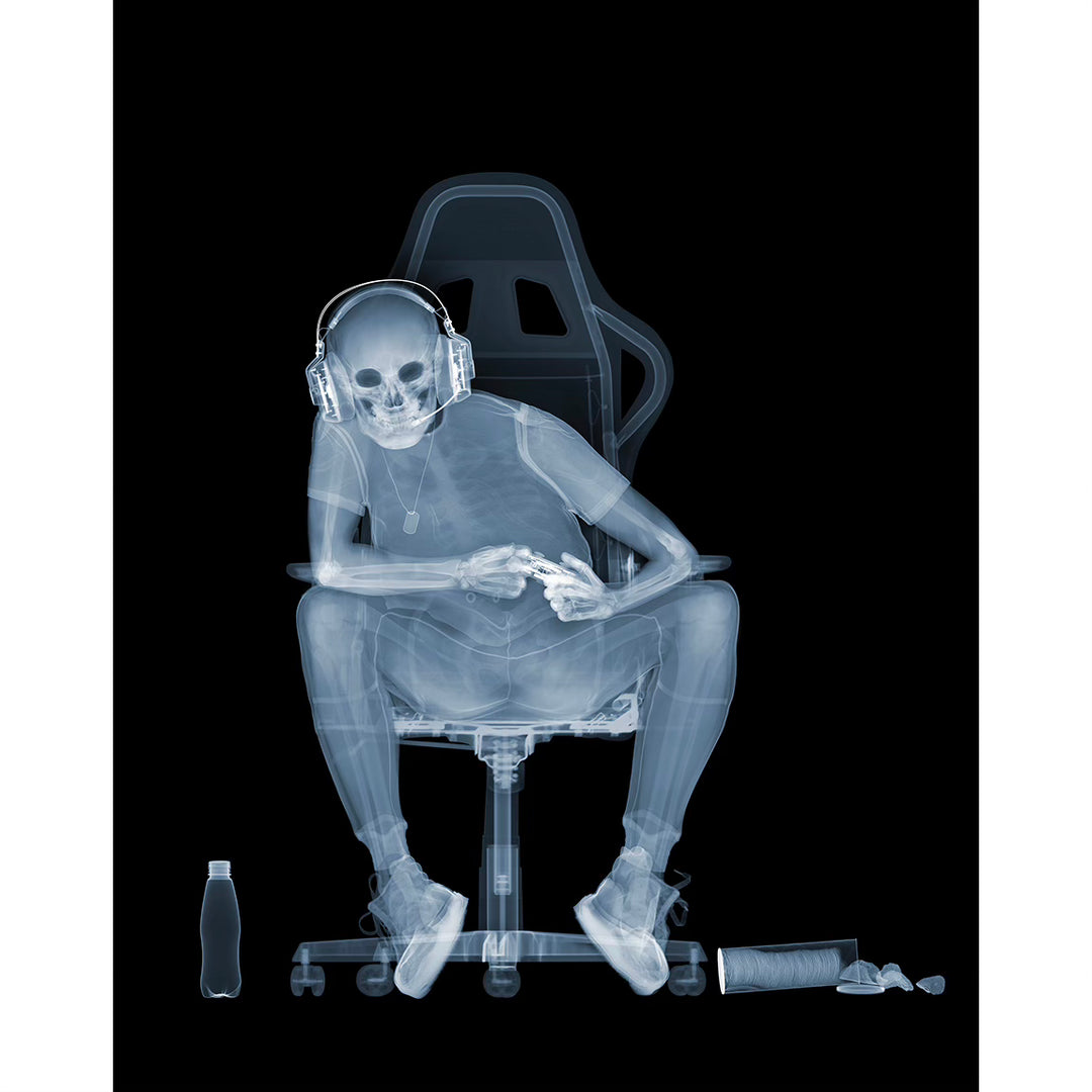 skeleton figure x ray photograph sitting in video gaming chair with headset and snacks in blue grey on black background