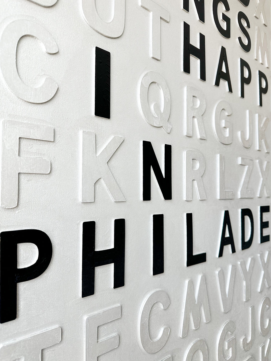 Steffanie Gerkin’s Bad Things White 3D is a contemporary mixed-media typography artwork made with raised wood and acrylic letters on canvas, featuring a white alphabet grid with bold black letters that spell “Bad Things Happen in Philadelphia.”