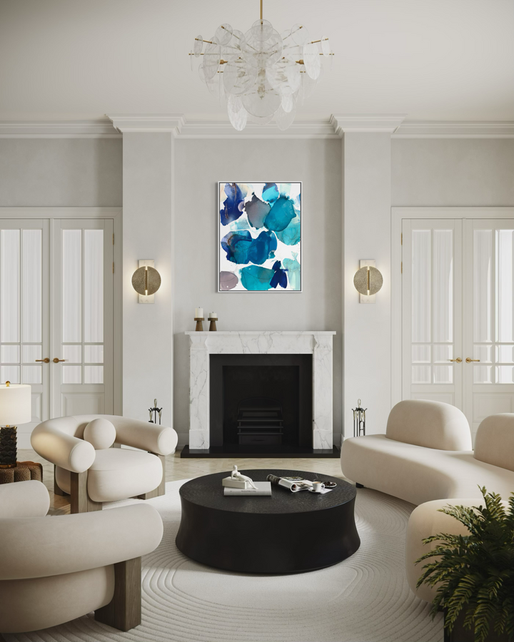 Framed "Blue Beach Glass 1" painting by Liz Barber displayed above a marble fireplace mantel in an elegant living room with cream sofas and a chandelier