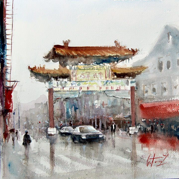 Chinatown arch over street with car driving beneath it in reds and yellows with washy blue buildings in background