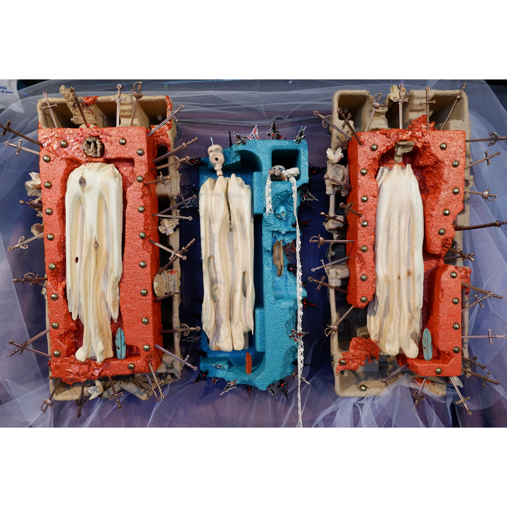 cartons with wooden carved figurines and metal sword crosses sticking out on top purple and white tulle fabric red and blue paint idols