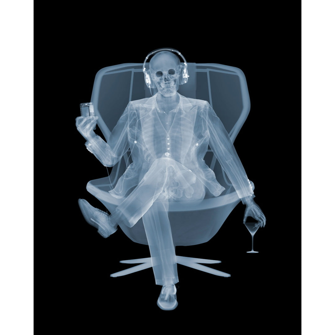 Framed Chromaluxe x-ray photograph by Nick Veasey of a skeleton listening to music with headphones in a swivel chair with a martini