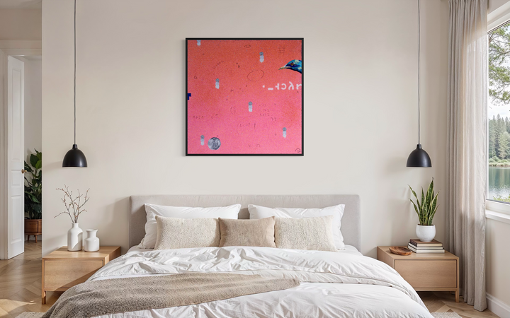 Bob Landstrom, Ethosien, pigmented volcanic rock and acrylic on canvas, 36 x 36 inches. Coral pink background with scattered small white and gray marks, handwritten symbols, an iridescent blue bird head at the right edge, and a gray circle at lower left, shown in a black frame above a bed with a beige upholstered headboard between two black pendant lights.