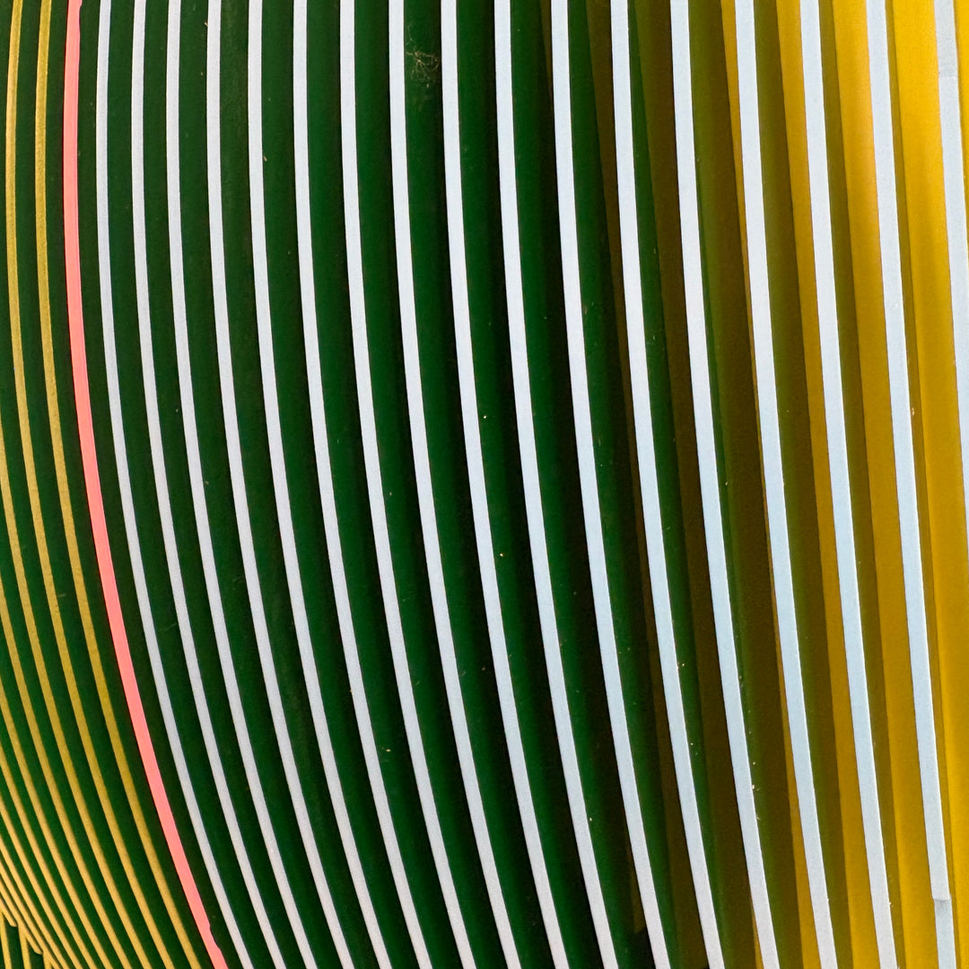 vertical stripes in green and blue with half split background in triangles on green and blue circular shape con-vexing sculptural out of center composition one pink line in middle