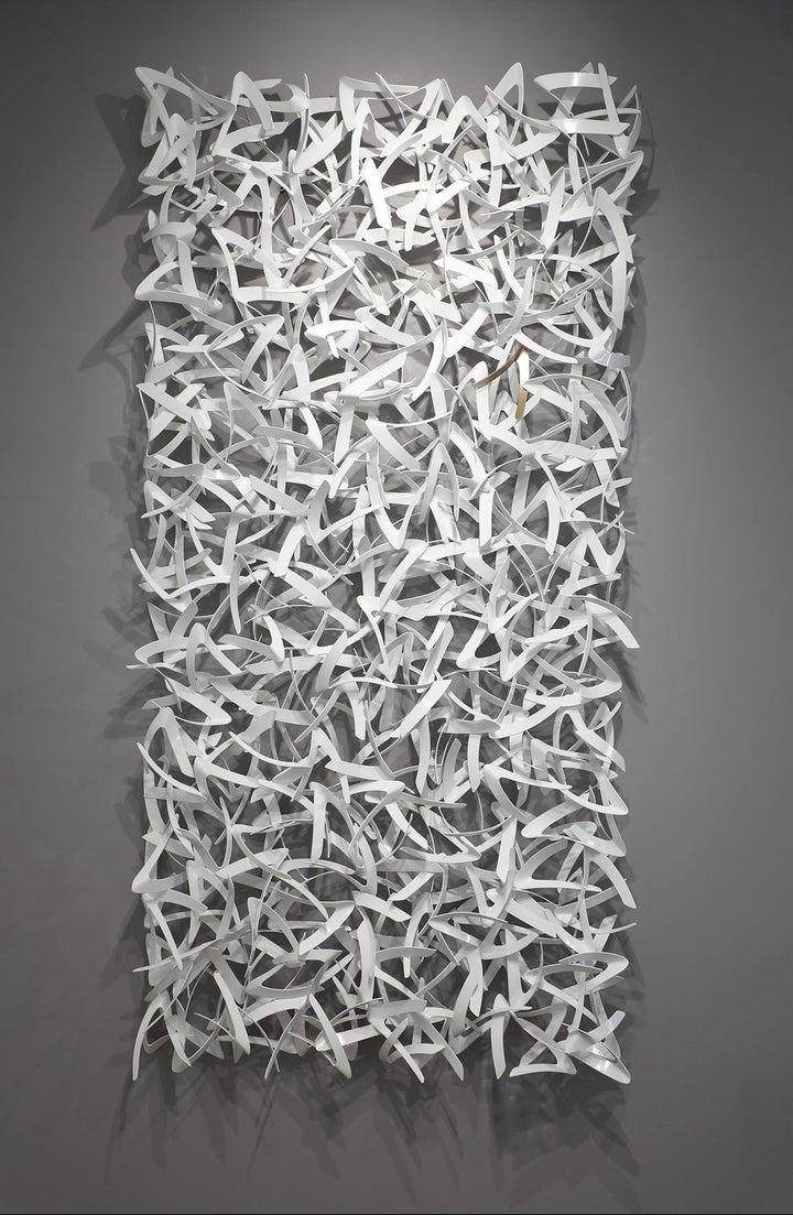 Matt Devine, Avian, powder-coated aluminum, made to order from 11 to 84 inches. Tall vertical rectangular wall sculpture of many small, curved white aluminum pieces shaped like bird wings, interlocked in a dense field on a grey wall.