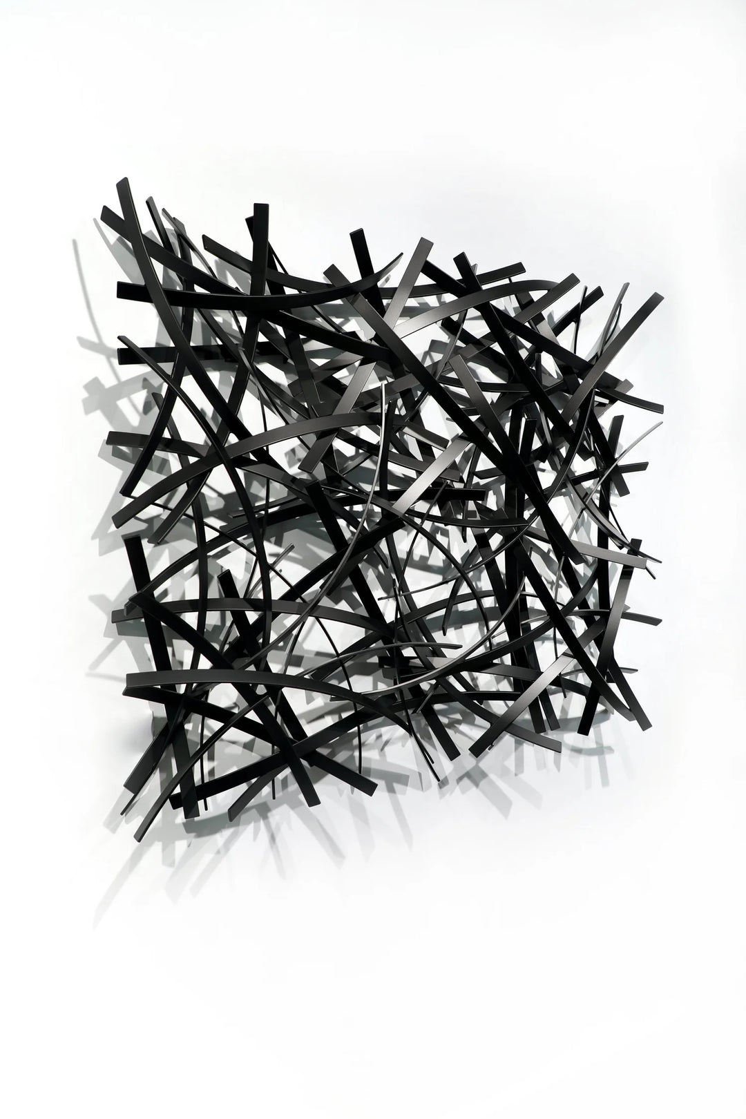 Matt Devine, Thin Bands, powder-coated aluminum, made to order from 11 to 84 inches. Square wall sculpture of thin, curved black and grey aluminum strips layered in a dense crisscross pattern on a white wall.