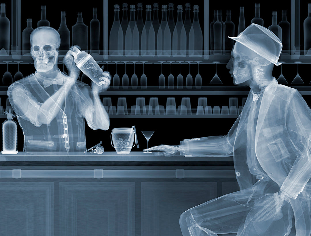 Framed Chromaluxe black and white x-ray photograph by Nick Veasey of two skeletons. A bar tender making a cocktail for a customer sitting at a bar with glasses and bottles behind them