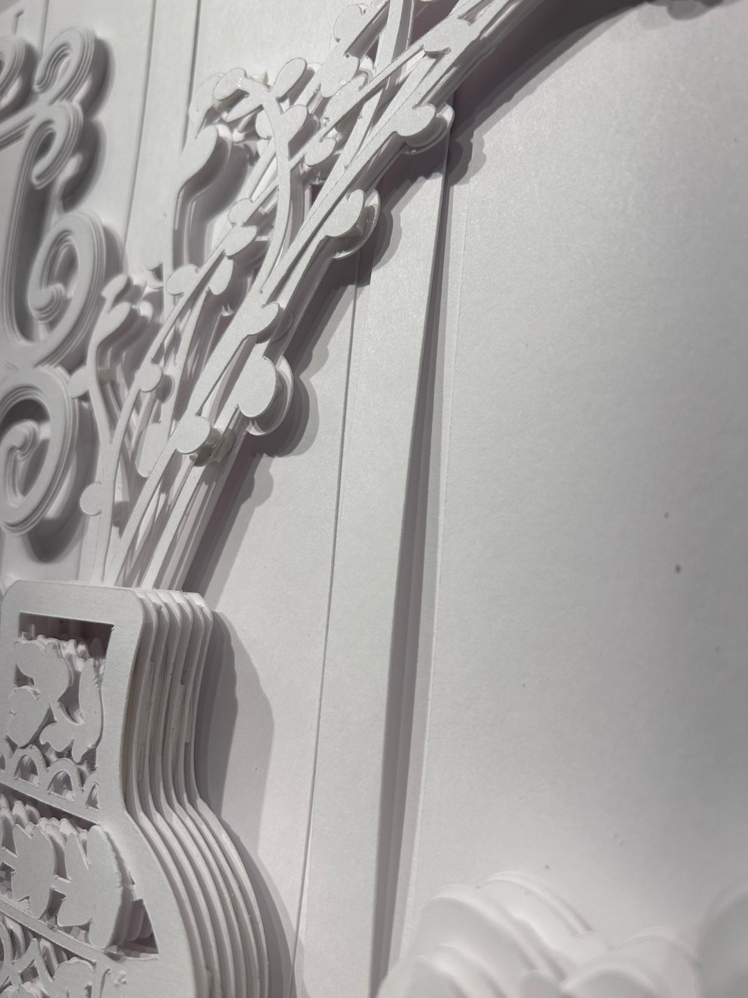 14"x14" layered white paper forming a vase with branches over a wall. 