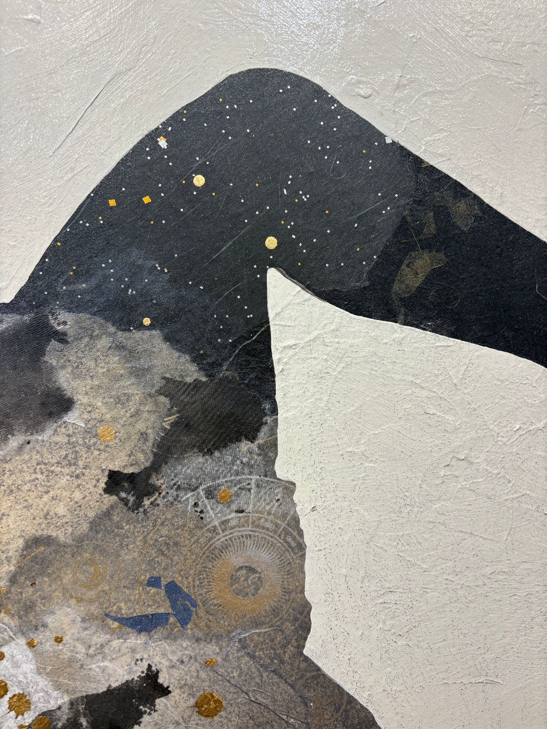 Close-up detail of Swinging Silhouettes II showing a charcoal-black leg and lower body section with scattered gold leaf flecks, contrasted against the heavily textured white canvas, with an ornate circular embossed paper element below.