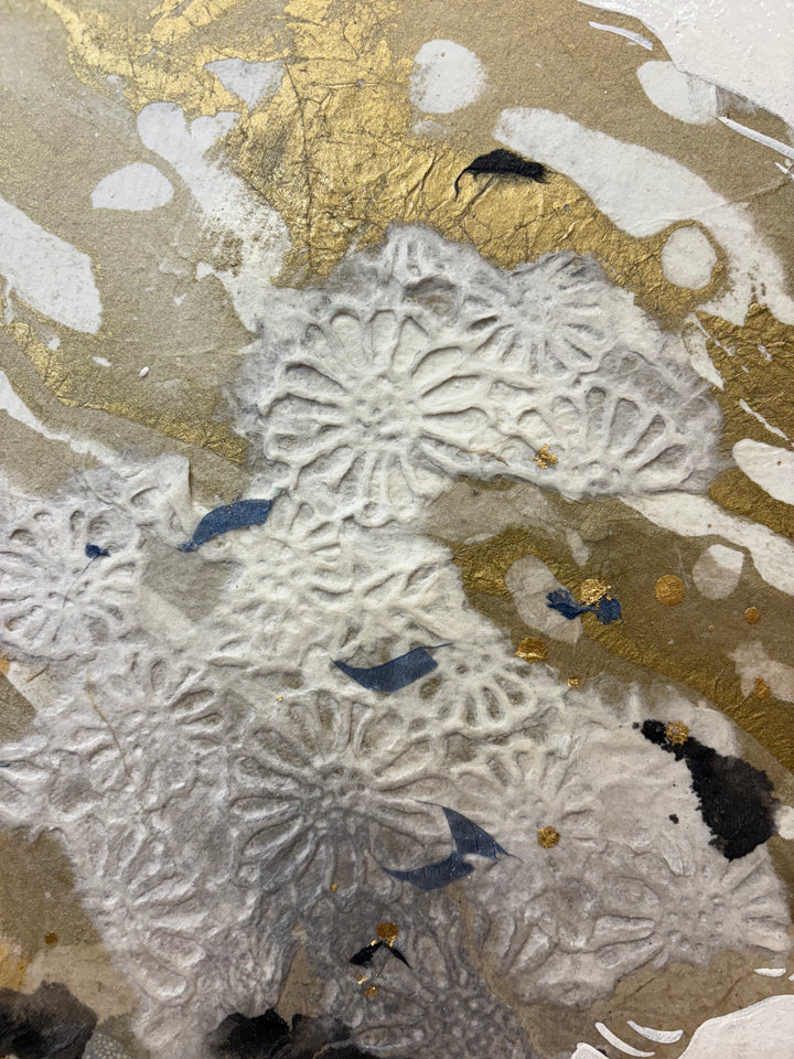 Close-up detail of Swinging Silhouettes II showing embossed white chrysanthemum-patterned paper elements set against rich gold leaf, with dark navy charcoal accents highlighting the ornate handmade paper collage.