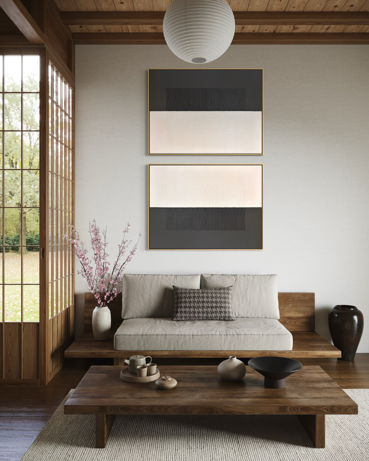 Lee in Cerulean, Split Duo Plain, joint compound and acrylic paint on canvas, 48 x 36 inches each (48 x 72 inches together). Two charcoal and cream textured panels stacked on a wall above a low wood-framed sofa in a room with wood ceiling beams, a paper pendant lamp, a wood coffee table, and a vase of pink blossoms.