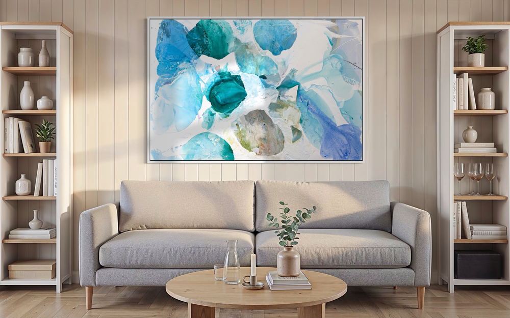 Liz Barber, Summer Garden 10, acrylic paint, ink, watercolor, and graphite on canvas, 72 x 48 inches. Horizontal abstract composition of overlapping translucent shapes in turquoise, teal, sky blue, and periwinkle with a sage and beige shape near the center, on a white background, shown in a white frame above a light gray sofa between white bookshelves with a round wood coffee table.
