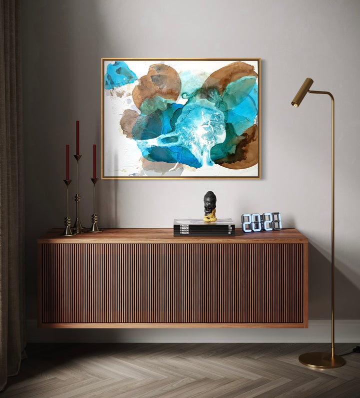 Framed "Surf" painting by Liz Barber displayed above a wooden credenza in a modern entryway with a brass floor lamp and candlesticks