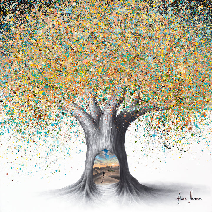 Ashvin Harrison, Tree of the Desert Oasis, coconut charcoal dust and acrylic on canvas, 36 x 36 inches. A grey charcoal-drawn tree with a thick trunk and spreading roots, its canopy made of turquoise, gold, peach, orange and black paint splatters on a white background, with an arched opening in the trunk showing a small figure walking across desert dunes toward green palms, mountains and a sunset sky.