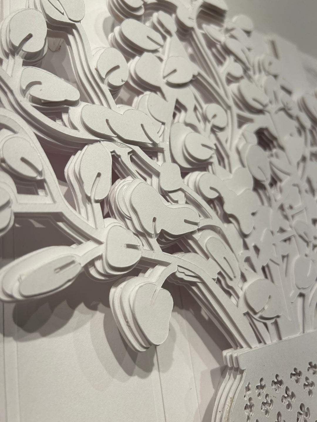 14"x14" layered white paper forming a vase with a fern over a wall.  